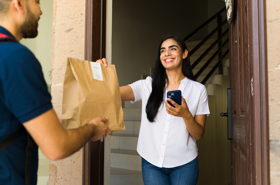 Woman accepting bag of food delivery at her front door.