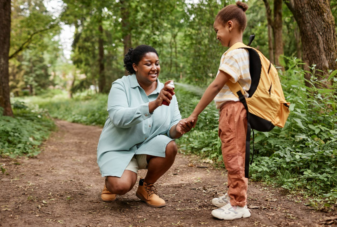 Mother spraying young child with bug repellant on trail in the woods.