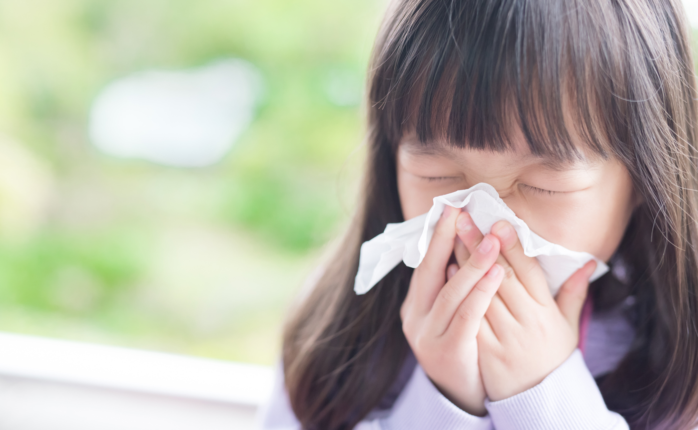 Young girl sneezing into tissue.