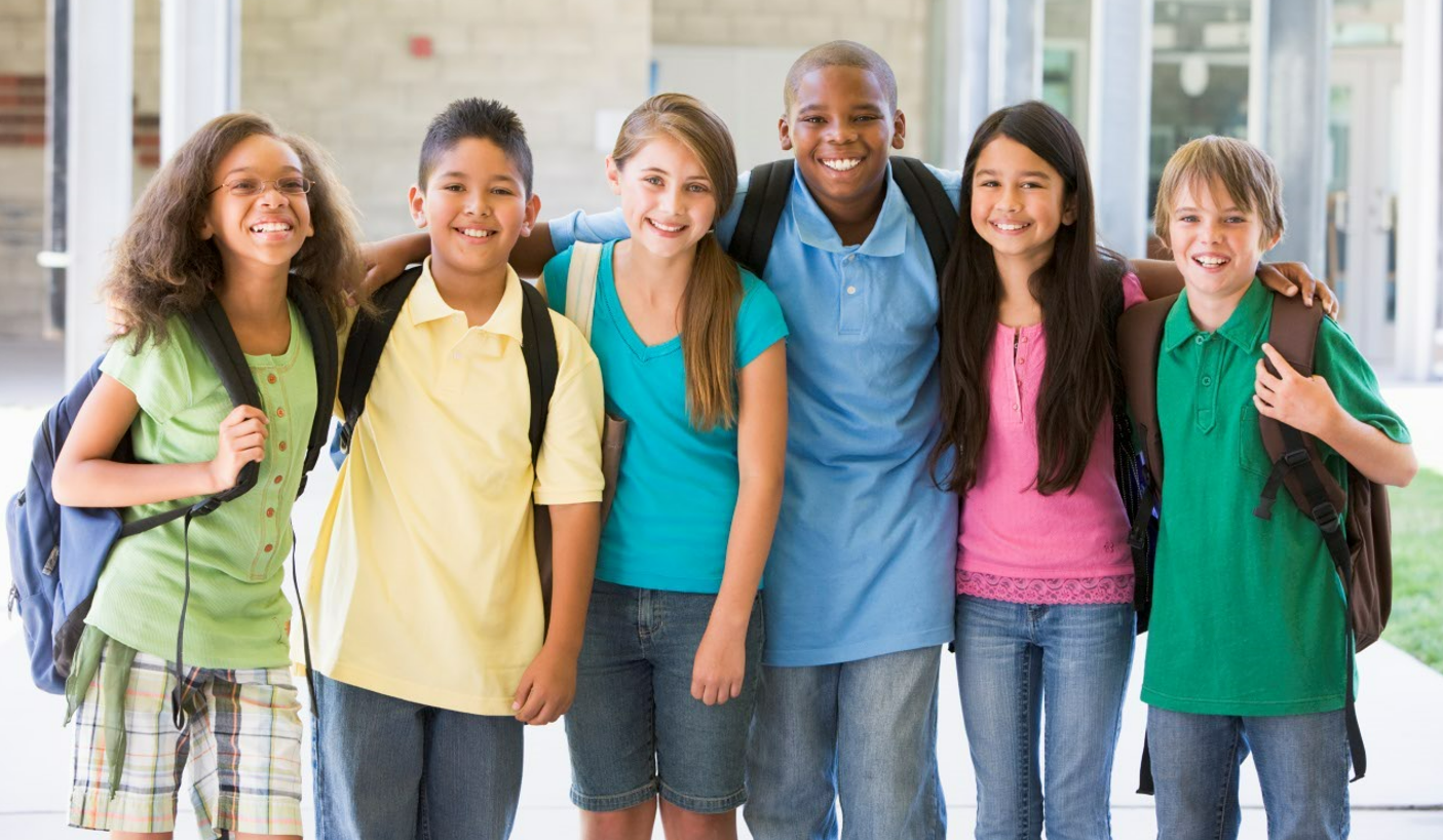 Group of older students wearing backpacks and posing arm in arm on campus..