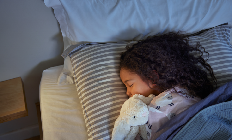 Young girl sleeping in bed holding onto stuffed bunny.