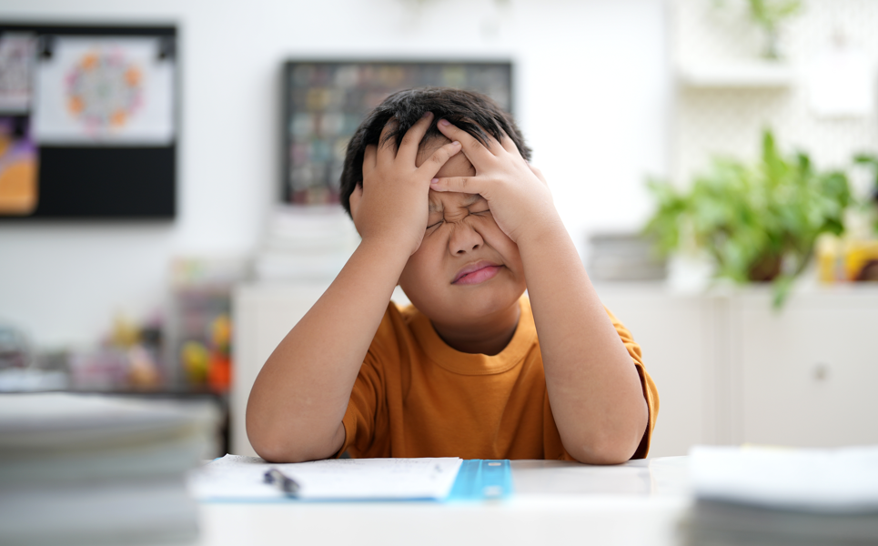 Young boy at desk holding head in hands in frustration.