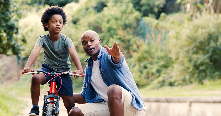 Man assisting young boy ride bike.