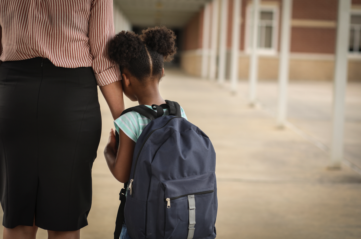 Young girl with mom hesitantly heading into first day of school
