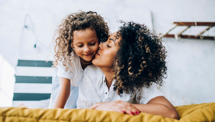 Mother kissing cheek of her young daughter.